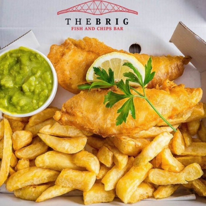 a golden fried fish with crispy chips, mushy peas and parsley in a box 
served at the brig takeaway in Dunfermline   